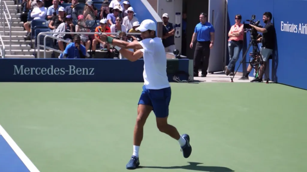 A player completing the forward swing of a two-handed backhand with full extension through the contact zone