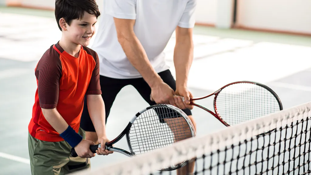 Young kids learning tennis on court with a coach
