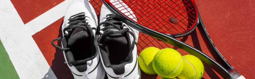 tennis racket, balls, and shoes laid out on court