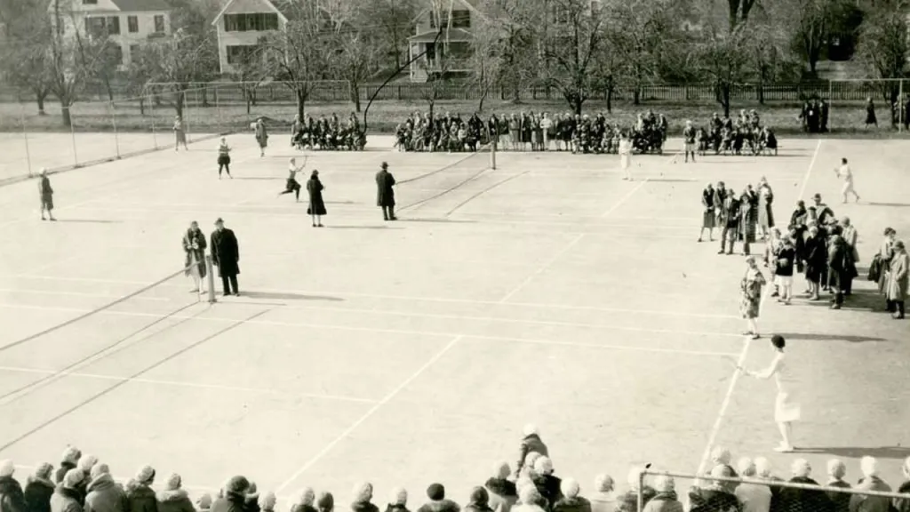An early tennis match from the Victorian era played on a grass court in a residential park setting